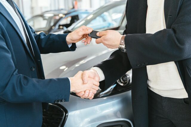 people shaking hands in front of a new car